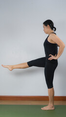 Obraz premium Asian young woman wear a black yoga outfit . Practicing yoga Standing Asanas Action UTTHITAHASTA PADANGGUSTHASANA D (Extended hand to big toe pose) .Home yoga practice on white background