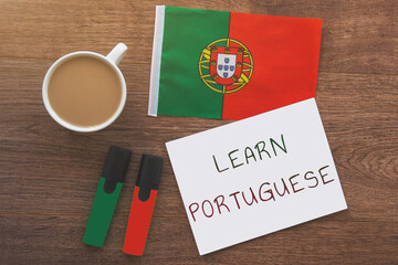 portugal national flag, notebook with inscription learn portuguese two markers, cup of coffee, pen on brown wooden desktop, learning concept