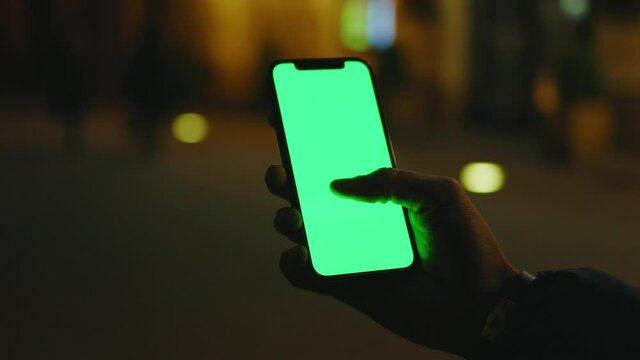 Slow motion hands man use phone with vertical green screen stand at night city street. Evening smartphone display application. Technology touchscreen cellular. Close up