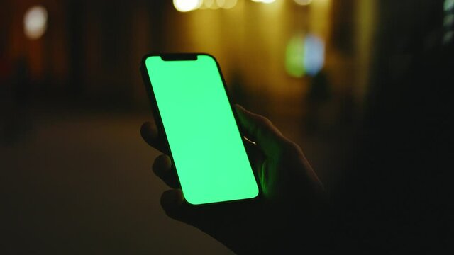 On street hands man use phone with vertical green screen stand at night city. Evening smartphone display application. Technology touchscreen cellular. Slow motion