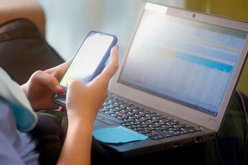 Side view of a young woman hand using smart phone and netbook to work from home. Selective focus