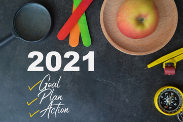 Selective focus of magnifying glass, ice cream sticks, apple, math compass and magnetic compass over black background written with 2021 GOAL , PLAN and ACTION. 