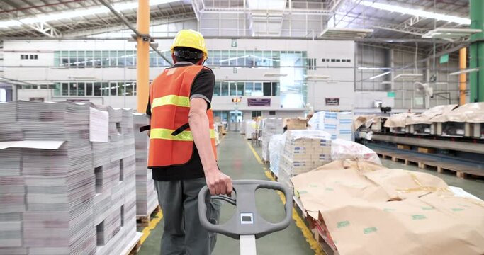 Warehouse worker pulling a pallet truck in industrial factory or warehouse.