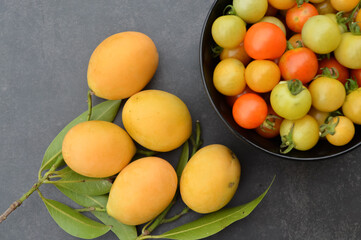 Bunch of fresh Bouea macrophylla or popularly known as marian plum, kundang or plum mango with cherry tomatoes or the scientific name called as Solanum lycopersicum over black background