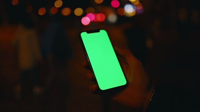 Hands man use phone with vertical green screen stand at night city background car. Evening smartphone display application. Technology touchscreen cellular. Slow motion