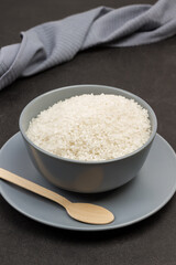 White round rice in gray bowl. Wooden spoon on gray plate. Gray towel on table
