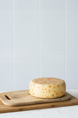 Whole cheese head of hard cheese parmesan on a wooden board with ceramic tile in background. Selective focus, vertical orientation, copyspace