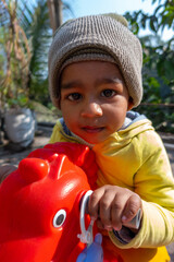 Little smiling baby boy sitting on a red toy horse in the winter sunny morning. Horse toy for preschooler and toddler children.