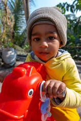 Little smiling baby boy sitting on a red toy horse in the winter sunny morning. Horse toy for preschooler and toddler children.