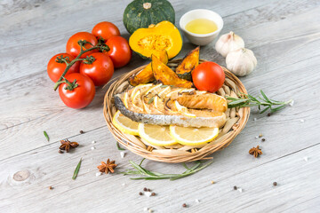 Grilled salmon steak on vintage wooden board with fork, olive oil, vegetables, herbs and spices on dark concrete background. Raw salmon fillet with vegetables, spices and lemon on wooden table.