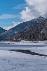 Fototapeta na wymiar Verschneite Berge am gefrorenen See im Chiemgau bei blauen Himmel mit Wolken