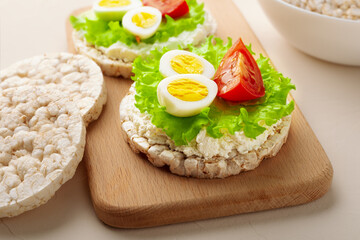 Close up rice cakes with cream cheese and quail eggs with lettuce and tomato on cutting board