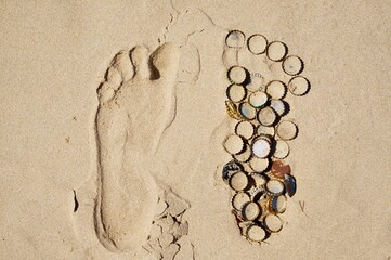 Thrown away beer bottle caps in a footprint in the sand on a beach