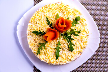 Mimosa salad beautifully decorated with carrot flowers on a white plate top view.