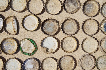 Rusty discarded beer bottle caps in a grid on a sandy beach