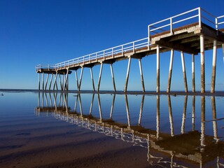Shallow water at low tide reflects a white wood pier - Hervey Bay