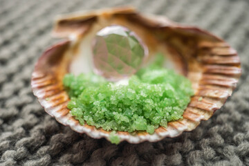 green sea salt and pink crystal in a seashell on a gray knitted surface