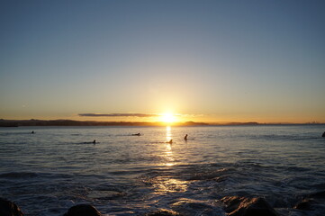 Fototapeta na wymiar The setting sun reflects off the calm ocean surface as surfers wait - Gold Coast