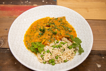 A plate of delicious chicken tikka masala and rice with peas on a wooden kitchen work top background