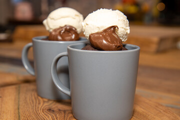 A cup of chocolate cake that has been made in a microwave with chocolate source and ice cream on a wooden kitchen work top