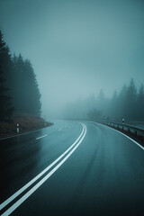 A moody and rainy view of a curved mountain road on a cold winter day with bad weather and heavy...