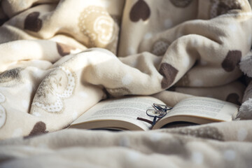 Cozy blanket, open book and reading glasses: concept image for cozy at home or lockdown