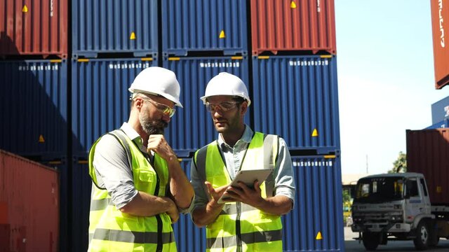 Two Foreman control loading containers box in container yard from cargo freight ship. Container ship in import and export business logistic company. Business Logistics and Transportation concept.