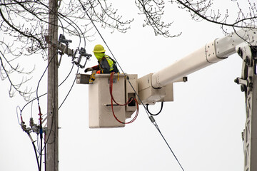 electrician in lift bucket repairing power transformer on a wooden pole outdoors