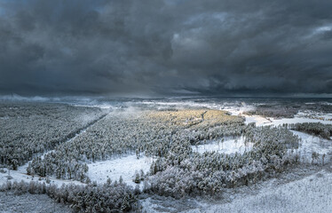 Snowy winter landscape with forest covered in snow. Aerial view over dramatic storm clouds. White scenic countryside.