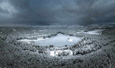 Snowy winter landscape with forest covered in snow. Aerial view over dramatic storm clouds. White scenic countryside.