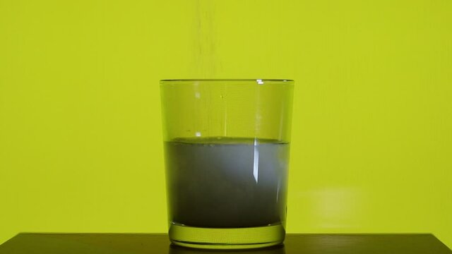Pour the magnesium citrate effervescent powder into half a cup of water on a yellow background