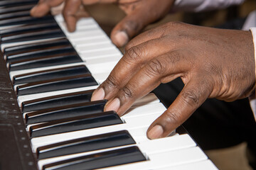 Fingers of an old African American man playing a keyboard piano wearing a black suit and pink shirt © Duncan
