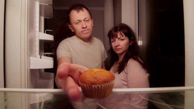 A married couple stands at an open refrigerator, spoiled food is on the shelf