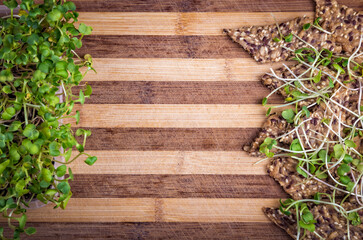 Crunchy crispy seed homemade bread decorated with microgreen sprouts and growing microgreens on a striped cutting board. Close up flat lay view. Copy space for text.