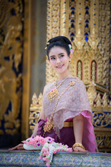 Beautiful Thai woman wearing a Thai Chitralada dress holds a garland in her hand in a Buddhist temple in Thailand which is architecturally beautiful.