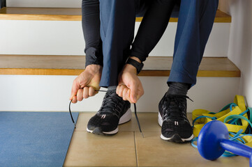 The young man is preparing for morning sport at home and laces sneakers sitting on stairs. Fitness...