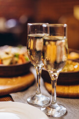 Close up of hands holding wine glasses and clinking against the backdrop of bright Christmas tree and burning fireplace, couple celebrating at Christmas table