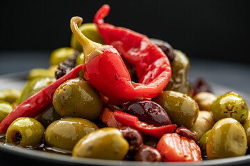 Delicious mixed olives and peppers in a plate with bread slice in the background.