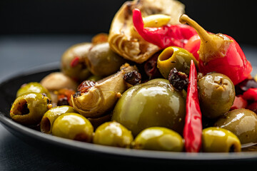Delicious mixed olives and peppers in a plate with bread slice in the background.