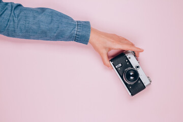 Female hand holding old retro photo camera on pink background with copy space for text. Trendy...