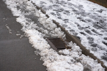12 - Highway surface drain surrounded by melting snow at the curbside