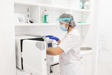 Sterilizing medical instruments in autoclave. Medical worker wearing protective facial mask face shield. Sterile medical tools.