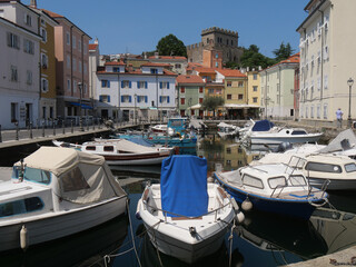 Obraz premium Mandracchio in Muggia : it is a small harbor inside the village and surrounded by ancient walls and colorful buildings. There are colored boats moored and reflected in the water.