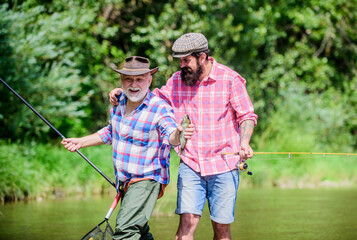 funny fishing. male friendship. family bonding. two happy fisherman with fishing rod and net. father and son fishing. summer weekend. mature men fisher. hobby and sport activity. Trout bait