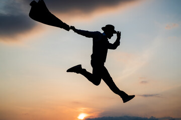 jumping man silhouette with hat and jacket dance against sunset sky, free