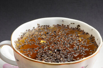 Close up view of tea cup isolated on a black background. Tea leaves on the surface of the water.