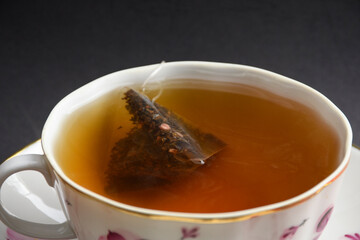Close up view of tea cup isolated on a black background. Teabag in the water. Hot beverage. 