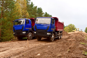 Dump trucks work on road construction in a forest zone. Tipper truck transport sand for roadworks project