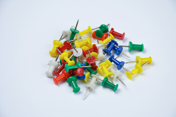 Plastic thumbtack pins of different color laying on a white paper.