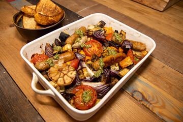 A baking trey of sausages and vegetables with tarragon relish